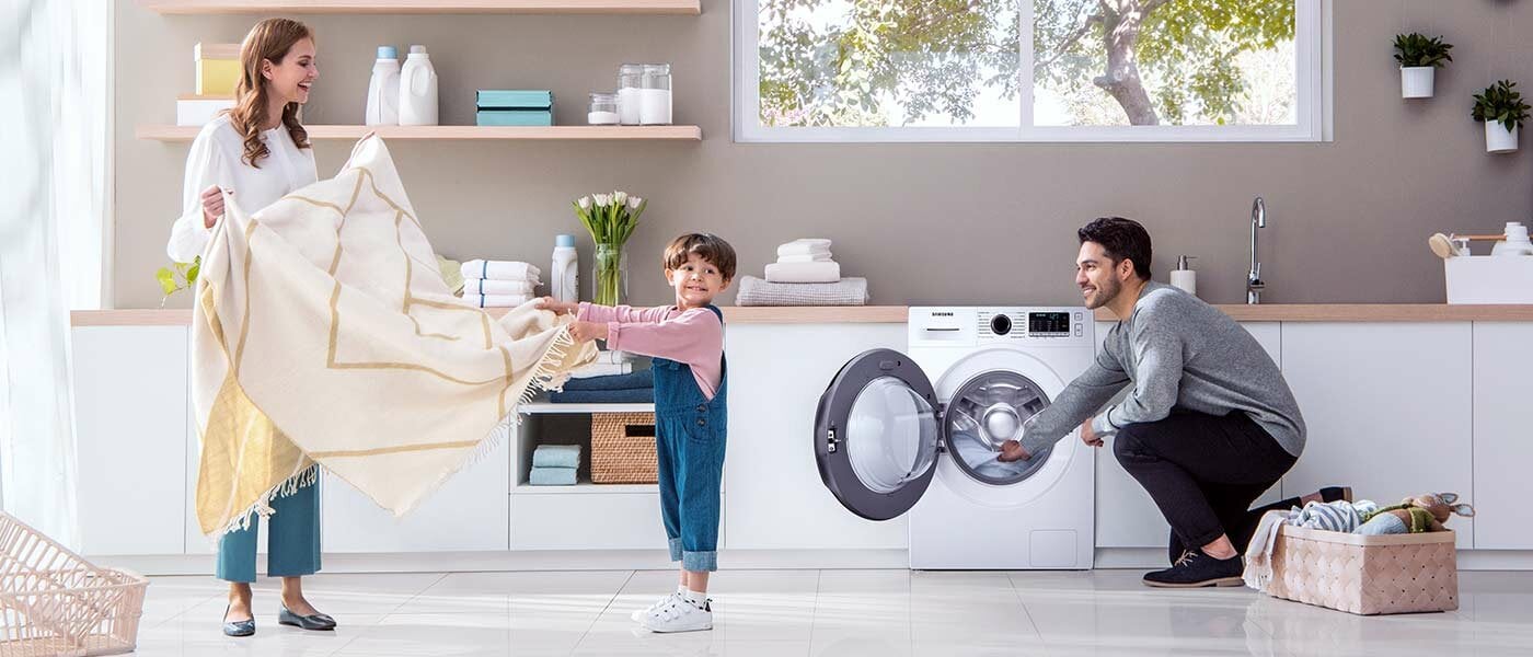 Rodzice z dzieckiem wyjmują pranie z pralki 