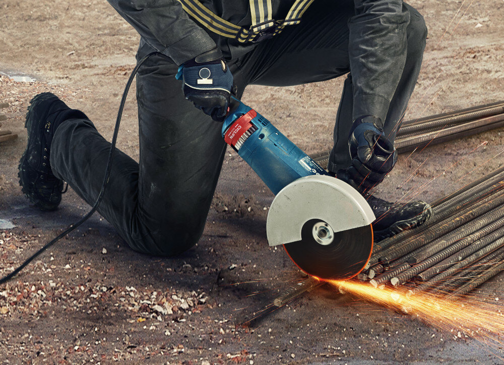 Szlifierka kątowa BOSCH GWS 24-230 P osoba trzyma szlifierkę w dłoniach tnąc metalową rurkę ergonomiczna konstrukcja rękojeści wygodna obsługa ergonomiczna rączka o bardzo małym obwodzie miękka powłoka typu SoftGrip stabilny chwyt
