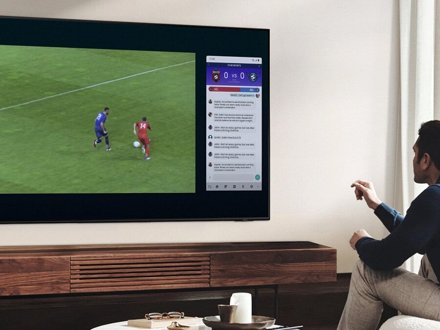 Mężczyzna korzysta z funkcji QLED Multi View, by oglądać mecz piłki nożnej i czytać wiadomości na tym samym ekranie, w tym samym czasie. Q77BATXXH