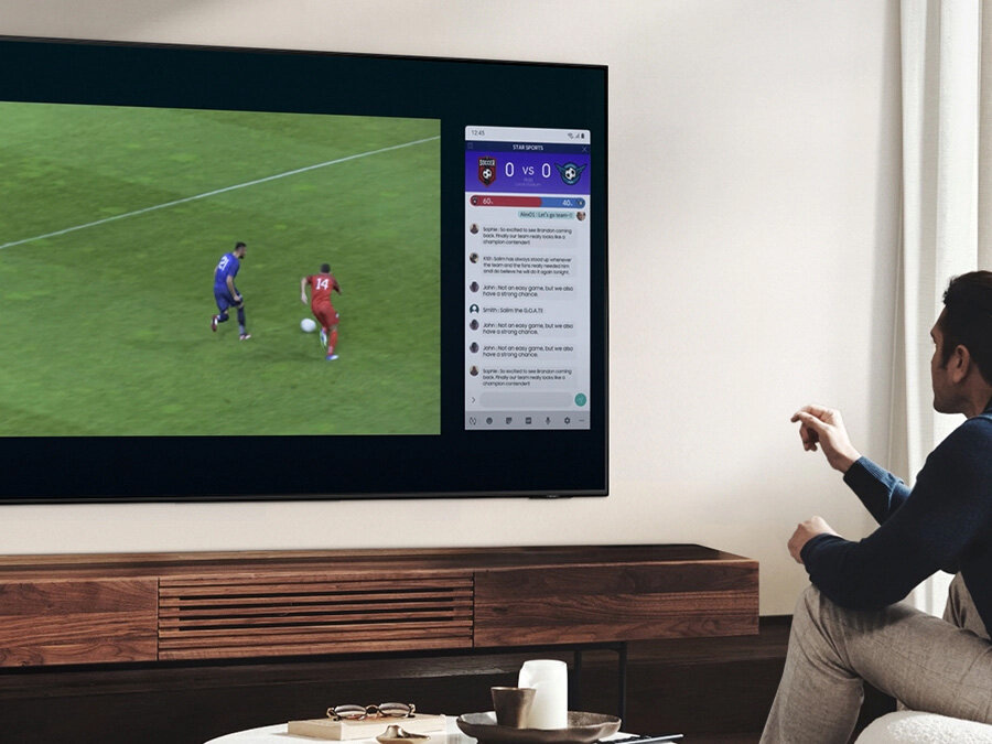 Mężczyzna korzysta z funkcji QLED Multi View, by oglądać mecz piłki nożnej i czytać wiadomości na tym samym ekranie, w tym samym czasie. Q70BATXXH