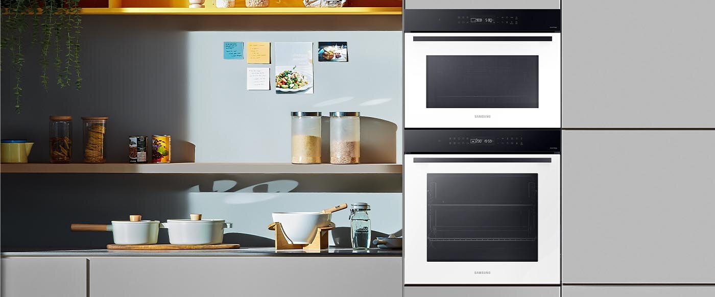 Dwa piekarniki Samsung wstawione do pomieszczenia kuchennego o szaro-niebieskich barwach.