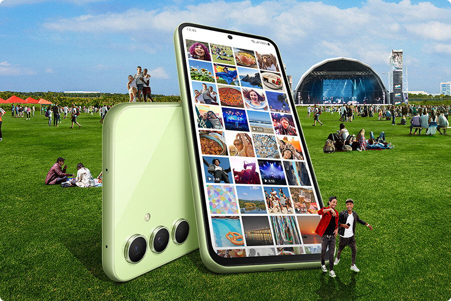 Na zewnątrz przy sali koncertowej wiele osób siedzi na trawie. Na pierwszym planie, dwa duże Galaxy A54 5G w w kolorze limonkowyn znajdują się również  na trawie, nakładając się na siebie, aby pokazać zarówno tył, jak i przedni ekran. Na ekranie otwarta jest aplikacja Galeria, która pokazuje wiele zdjęć w swoim albumie. 