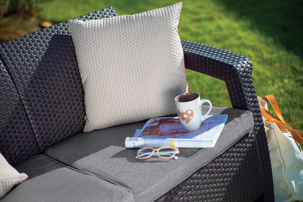 Sofa ogrodowa KETER Corfu II Love Brown 258946 Brąz zbliżenie na poduszki a poduszce gazeta filiżanka i dodatkowa poduszka dwie wygodne poduszki komfortowy odpoczynek łatwe utrzymanie czystości