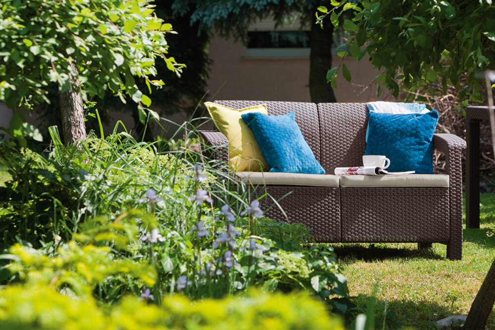 Sofa ogrodowa KETER Corfu II Love Brown 258946 Brąz sofa na trawie w tle rośliny i płot prosty montaż system JUST CLICK AND GO montaż na zatrzaski intuicyjny w obsłudze nie wymaga użycia dodatkowych narzędzi Intuicyjny system łączenia szybkie i proste złożenie sofy