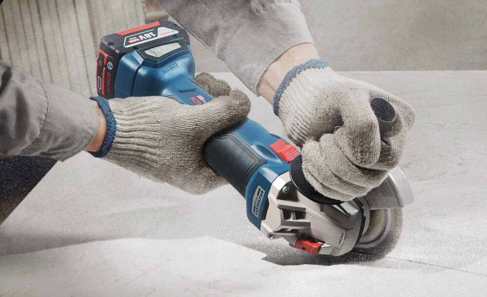 Szlifierka kątowa BOSCH Professional GWS 18V-10 P 06019J4101 osoba trzyma szlifierkę w dłoniach tnie beton bezpieczeństwo użytkowania wbudowany system zapobiegania przypadkowemu włączeniu po zaniku prądu ochrona przed przeciążeniem wyłącznik przeciążeniowy ochrona narzędzia przed przegrzaniem system Drop Control wysoki standard bezpieczeństwa