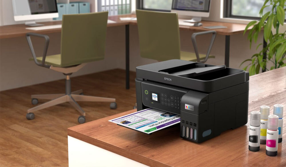 Багатофункціональний принтер EPSON EcoTank L5310. Кольоровий друк, презентація пристрою Wi-Fi на столі, надрукована на аркуші паперу, що виходить, поруч із пляшкою на задньому плані, столи, стільці та комп'ютери, економія коштів без картриджів.
