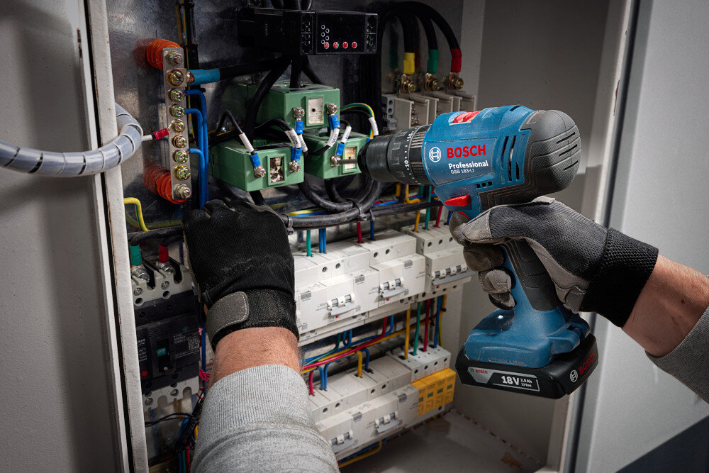 Wiertarko-wkrętarka BOSCH Professional GSB 183-LI 06019K9100 ściana skrzynka z czujnikami i kablami osoba używa wiertarko-wkrętarki akumulator 18 V praca bez przewodów kompatybilność ze wszystkimi akumulatorami i ładowarkami Bosch Professional 18 V w zestawie dwa akumulatory o pojemności 2,0 Ah i ładowarka