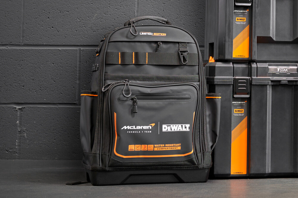 Plecak monterski DEWALT McLaren F1 DWST60122-1 plecak na tle ściany widoczny od przodu wysokiej klasy materiał o gęstości 1680 denier zabezpiecza plecak przed przetarciami wodoodporna komora o klasie IP54 chroni zawartość przed deszczem wilgocią i kurzem bezpieczny sprzęt
