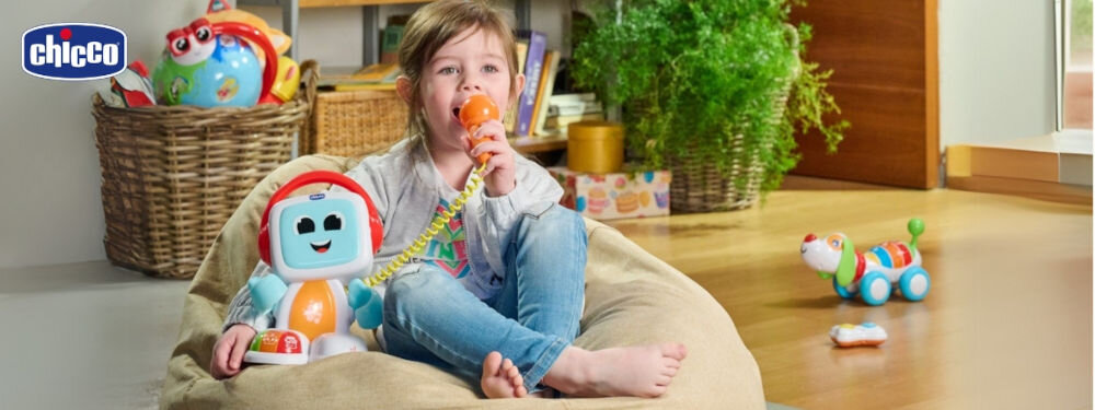 Zabawka edukacyjna CHICCO Happy Music Śpiewający robot Robit 00011853000000 dziecko siedzące z zabawką robota świecący brzuch zabawki przyciski na obudowie dziewczynka trzyma  w ręku pomarańczowy mikrofon i śpiewa Śpiewanie do mikrofonu wybór różnych gatunków muzycznych tworzenie zabawnych efektów głosowych wsparcie rozwoju mowy oraz wyobraźni motywuje do naśladowania dźwięków rozwój zdolności językowych i umiejętności komunikacyjnych stymulacja poczucia rytmu i koordynacji słuchowej 