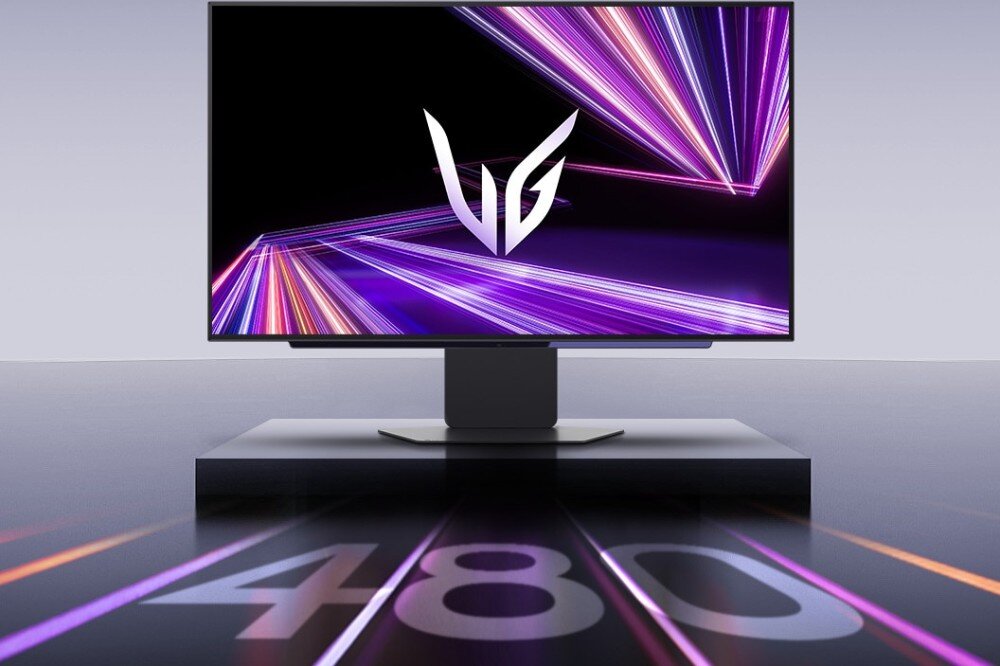 Monitor LG UltraGear 27GX790A-B.AEU Monitor z logo 'VG' na ekranie i dynamicznymi, kolorowymi smugami światła w tle. Na powierzchni pod monitorem widać duży napis '480', opis