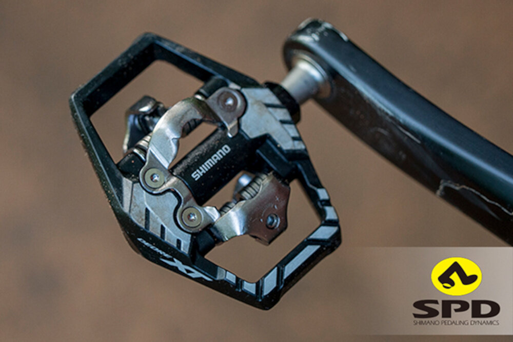 Buty rowerowe SHIMANO SH-RX600 Czarny rozmiar 47 brązowe tło widok na pedał od roweru w prawym dolnym roku napis SPD przystosowane do pedałów SPD pewne połączenie z rowerem i efektywne pedałowanie współpracują z modelami PD-M8100 oraz PD-ES600 stabilność i bezpieczeństwo