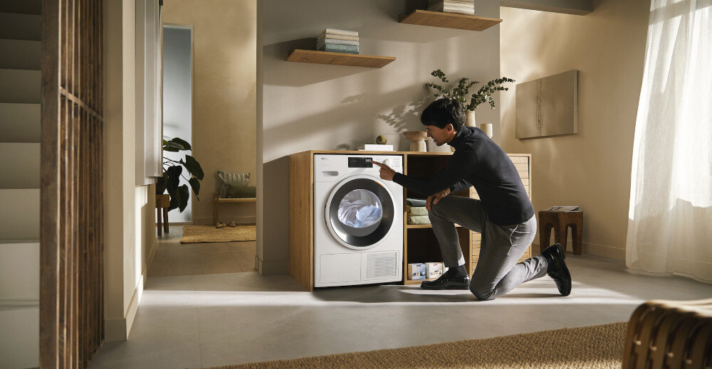 Suszarka MIELE TWC640WP EcoSpeed zdjęcie wizualizacyjne lifestyle pomieszczenie mężczyzna zmiana ustawień panel Optymalna ochrona domu optymalne wartości szczelności ochrona domu mebli pomieszczeń