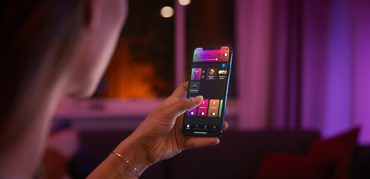 Taśma LED PHILIPS HUE 929003816902 3 m Bluetooth, aplkacje, aranżacje, światło, Hue, Kobieta trzyma w dłoni telefon z aplikacją w pomieszczeniu ze światłem philips
