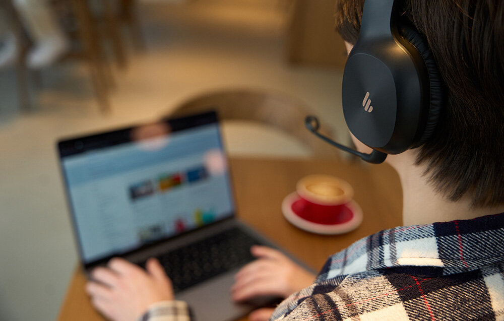 Słuchawki EDIFIER K750W Bluetooth 5.4 multipoint łączność stabilność, osoba z założonymi słuchawkami nausznymi pracująca na laptopie