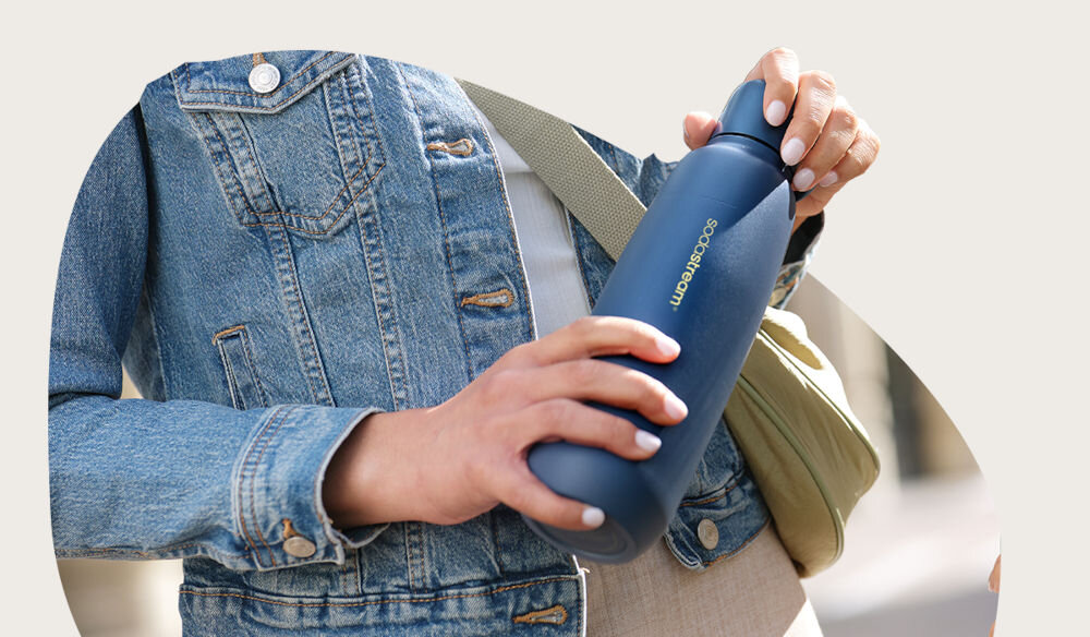 BUTELKA TERMICZNA SODASTREAM DO GAZOWANIA WODY STORM BLUE 0.9L osoba trzyma  w ręku butelkę w kolorze granatowym zakrętka uchwyt pojemność 0,9 l funkcjonalność bidonu kubka termicznego butelki do saturatora gazowanie wody bezpośrednio w środku podwójne ścianki do 12 godzin elegancja granatowy elegancki uniwersalny kolor wyrafinowany design funkcjonalność