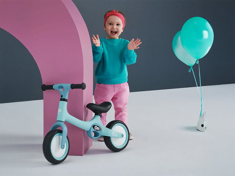 Rowerek biegowy KINDERKRAFT Tove Beżowy niebieski rowerek oparty o słupek gumowe uchwyty czarne siodełko obok stoi uśmiechnięte dziecko intuicyjny mechanizm montażu w zaledwie trzech prostych krokach kilka chwil przygoda na dwóch kołach wygoda dla zapracowanych rodziców praktyczny system składania bez zbędnych narzędzi i dodatkowych komplikacji