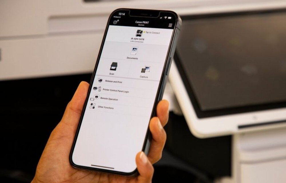 Багатофункціональний принтер CANON i-SENSYS MF463dw II, автоматичний двосторонній друк, Wi-Fi. Людина тримає смартфон із додатком для принтера, що показує опції друку, сканування та дистанційного керування пристроєм, керування додатком, підключеним до хмари.